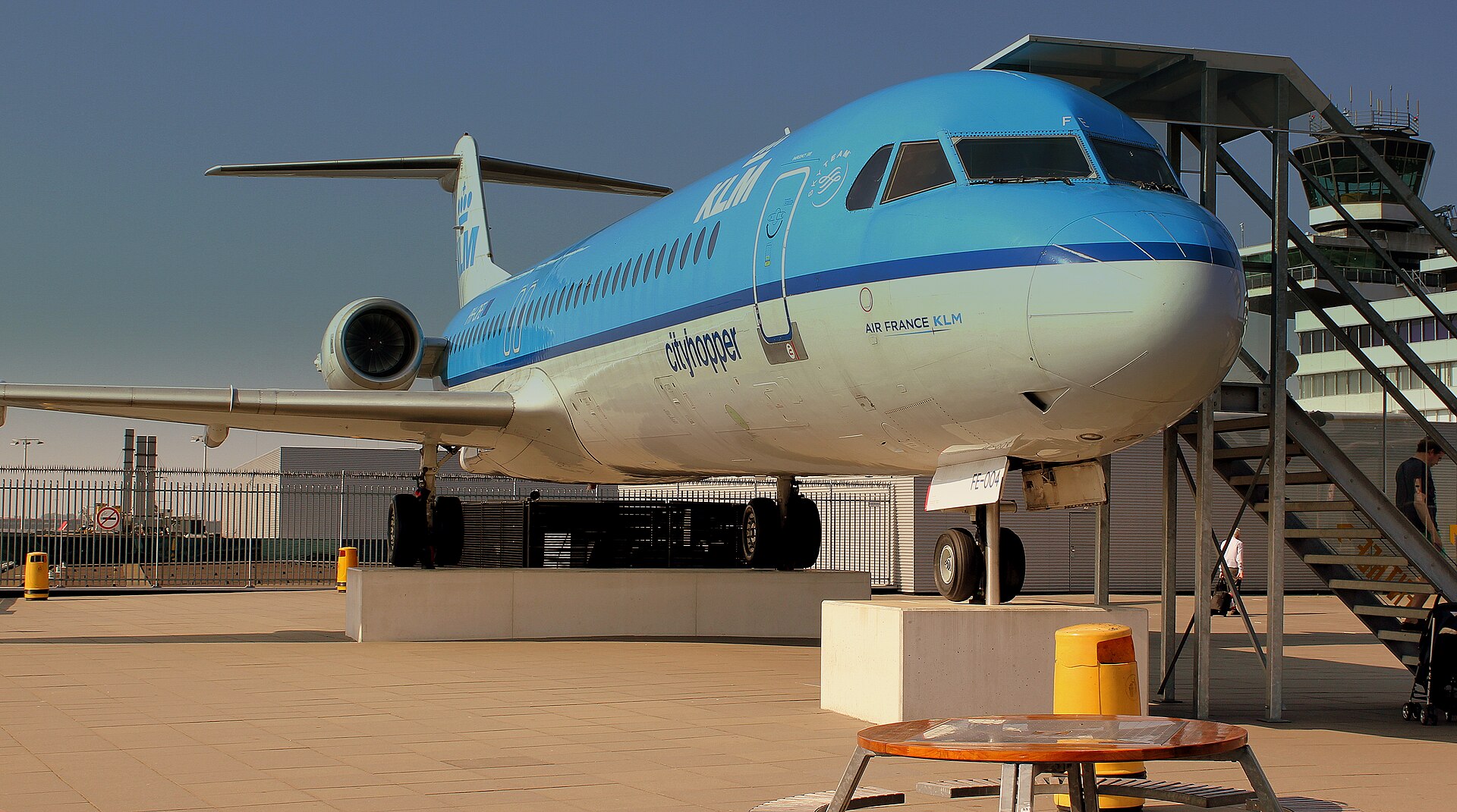 Retired KLM Fokker 100 PH-OFE displayed on Schiphol Airport’s Panorama Terrace, with visitor stairs beside the aircraft.