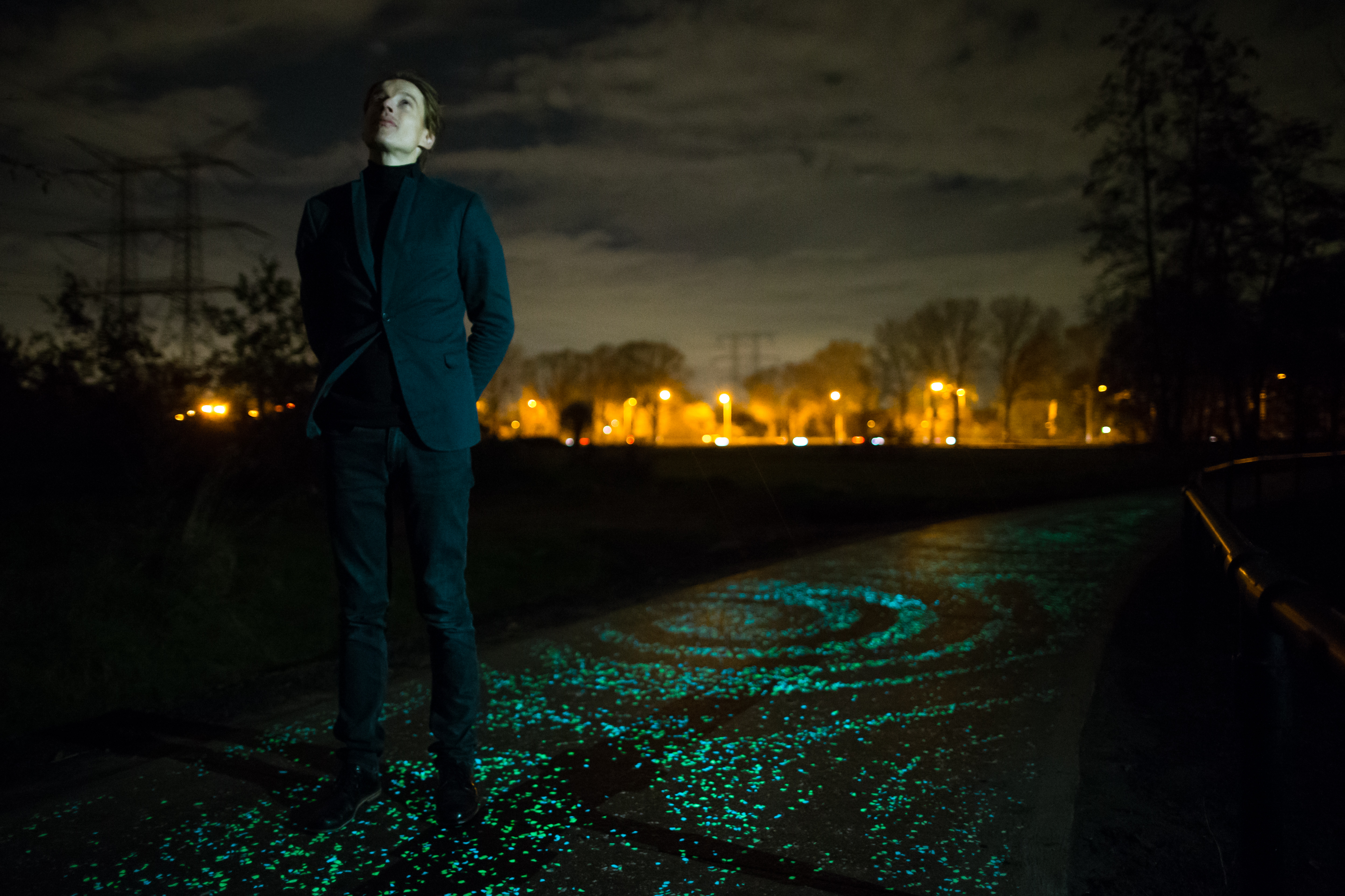 Cyclists ride through glowing blue-green patterns on the Van Gogh–Roosegaarde Cycle Path at night.